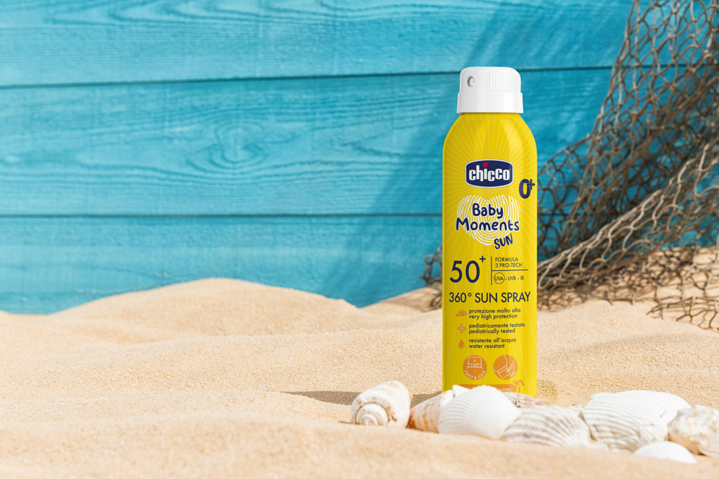 A spray bottle sunscreen sitting in the beach sand with weathered blue planks behind